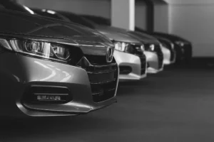 Row of modern sedans with close-up on the front bumper and grille, showcasing factory-finish detailing and alignment under indoor lighting conditions.