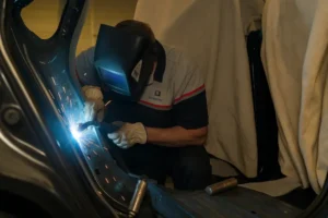 Technician wearing protective gear welding the inner structure of a car during structural reinforcement and realignment.